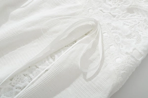 Close-up of intricate white lace embroidery and delicate ribbon tie on a stylish top