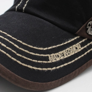 Close-up of baseball cap brim featuring triple beige stitching and metal badge detail