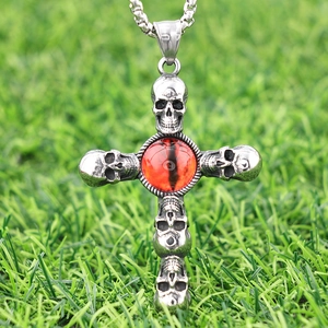 Macro shot of gothic cross skull pendant with red eye on green grass setting