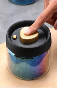 Close-up of hand pressing golden heart vacuum button on black glass canister lid