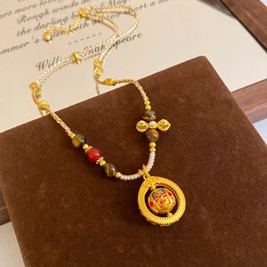 Detail of tiger eye and red agate beads on a golden necklace with traditional mask pendant