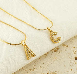 Close-up of gold-plated necklaces with diamond-encrusted A and C letter pendants