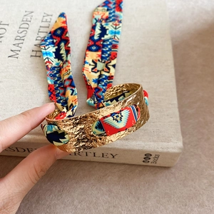 Close-up of golden hammered cuff bracelet with colorful bohemian silk fabric wrap detail