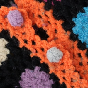 Close-up of handmade colorful crochet cardigan featuring 3D puff balls and hollow knit