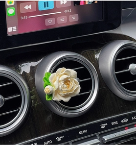 Detail of a white jasmine flower car diffuser clip mounted on the air vent with green leaves