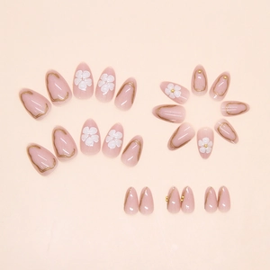Flat lay of pink almond press-on nails with white 3D flower petals and gold relief detail