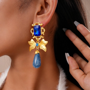 Macro detail of vintage gold bow earrings with navy blue gems and marble water drops