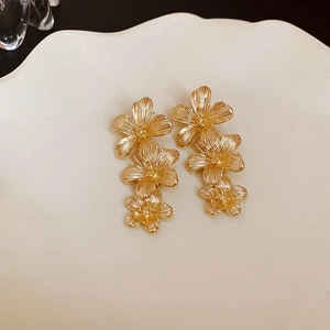Boucles d'oreilles fleurs dorées à trois couches sur plateau blanc et fond sombre chic