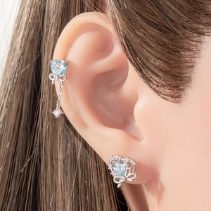 Silver bow heart earrings set with light blue zircon stones on a model ear