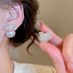 Close-up detail of silver bow earrings with micro-set stones and a large round pearl drop