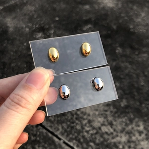Close-up of minimalist oval stud earrings in polished gold and silver finishes