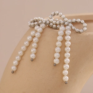 Exaggerated vintage 18K gold plated bow earrings with white pearl tassels on beige background