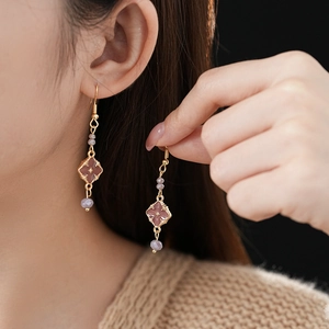 Detail of vintage gold-plated drop earrings with purple clover gemstones on a model