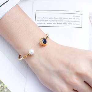 Elegant gold flower bangle with a white pearl and deep blue crystal on a model wrist