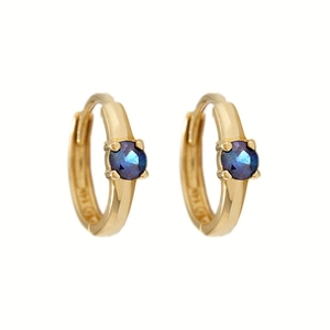 Detalle de pendientes huggie de oro de 14K con una piedra preciosa azul oscuro facetada