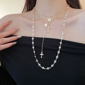 Close-up of layered cross and pearl pendants necklace on a model with black top