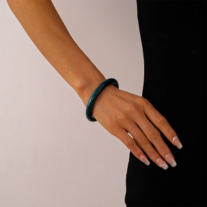 Close-up of a dark green acrylic bangle with natural ink-wash pattern on a female wrist