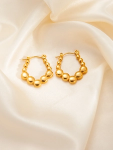 Detailed close-up of golden beaded hoop earrings with star elements on beige silk