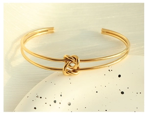 Dettaglio di un bracciale rigido dorato vintage con nodo intrecciato su un piatto bianco