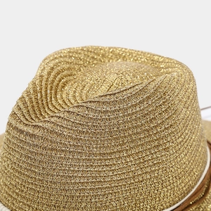 Macro shot of gold woven straw sun hat with metallic luster and brown leather decorative band