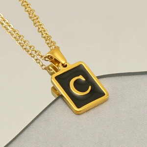 Détail d'un collier chaîne dorée avec pendentif rectangulaire noir orné de la lettre C