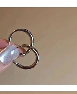 Detailed view of silver hoop earrings held by hand showcasing high-polish finish