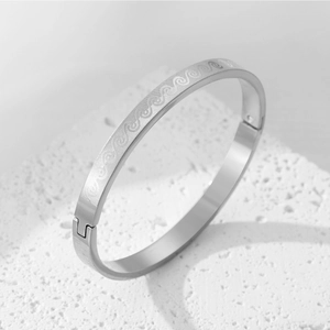 Detailed close-up of a silver titanium steel bangle with engraved wave patterns on a stone base
