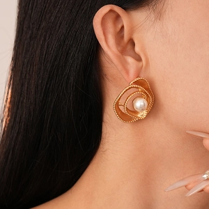 Close-up of golden spiral flower earring with white pearl on model's ear