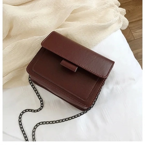 Detailed view of deep brown faux leather square bag with dark grey metal chain strap
