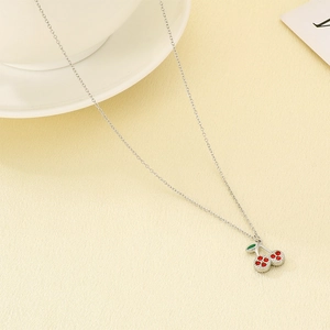 Macro detail of the silver chain with red rhinestone cherry pendant and green enamel leaf