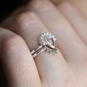 Macro shot of a teardrop-shaped faux moonstone crown ring set worn by a model