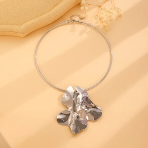 Detail of silver irregular crumpled pendant on minimalist choker necklace over beige background