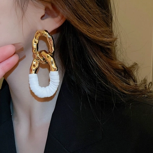Gros plan sur des boucles d'oreilles entrelacées en métal doré et similicuir blanc plissé
