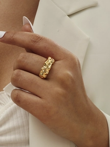 Close-up of a wide gold-plated wrinkled texture ring on model with white blazer