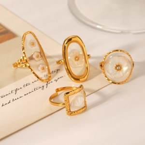 Close-up of gold-plated rings featuring white resin floral and shell motifs on light surface