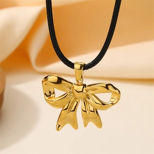 Macro shot of 18k gold plated bow pendant on black cord necklace over silk