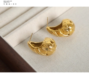Macro shot of gold teardrop earrings with woven texture on beige jewelry box