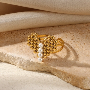 Detail of adjustable gold heart ring with four white pearls on a stone surface