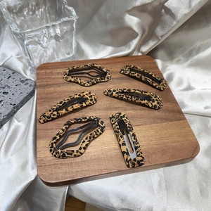 Macro view of six leopard print hair clips set on a wooden tray with elegant silk background