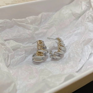 Detail of silver C-shaped earrings with wavy texture resting in a white jewelry box