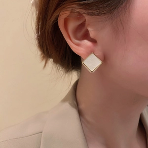 Gros plan de boucles d'oreilles géométriques carrées dorées avec insert blanc