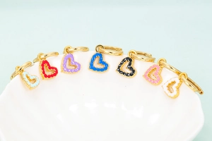 Detailed view of colorful enamel heart pendants on gold earrings hanging on a ceramic bowl