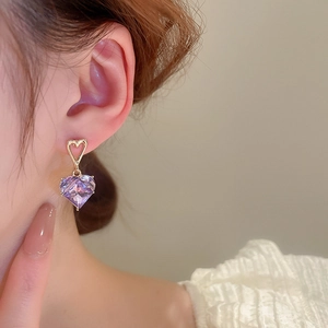 Detailed close-up of a purple heart crystal earring with a gold heart stud on a model