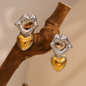 Macro view of unique lip and heart mixed metal drop earrings on a rustic wood stand