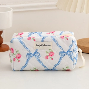 Detail of floral quilted makeup bag featuring blue bows and pink roses with a woven label