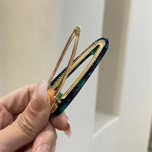 Green and blue marble acetate hair clip with golden metal clip shown in hand