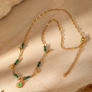 Detail of gold necklace featuring green stone beads and celestial charms on stone surface