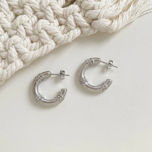 Boucles d'oreilles minimalistes argentées en forme de C avec cristaux sur fond blanc