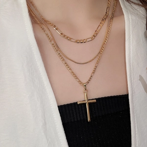Detail of layered gold Figaro chains and snake chain with a minimalist cross pendant