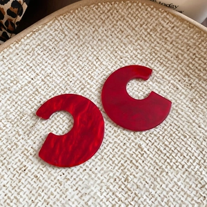 Detailed macro view of red marble acrylic C-shaped earrings on a stylish tray